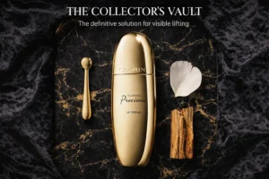 Clarins Precious Le Sérum in a streamlined golden bottle displayed on a polished marble vanity.