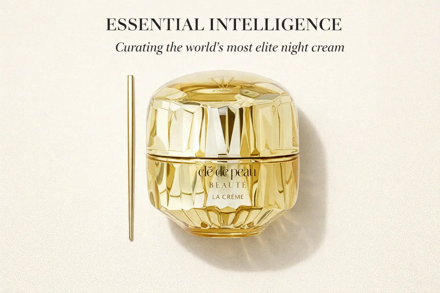 A luxurious gold multi-faceted jar of Clé de Peau La Crème sits on a polished marble surface.