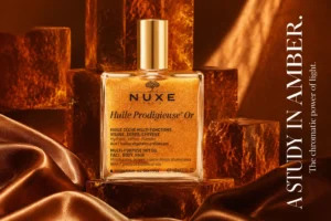 Square glass bottle of Nuxe Huile Prodigieuse Or showing shimmering golden dry oil with a gold cap.