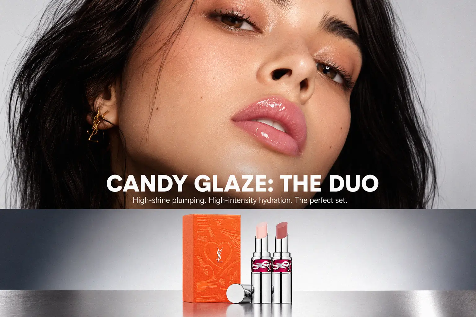 Two gold YSL lip gloss tubes standing on a white surface with a soft glossy reflection.