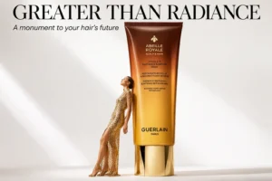 A premium double-chamber tube of Guerlain Abeille Royale hair mask on a white marble vanity shelf.