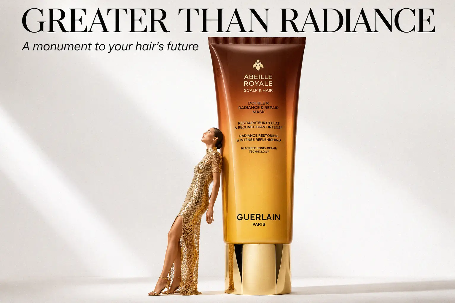 A premium double-chamber tube of Guerlain Abeille Royale hair mask on a white marble vanity shelf.
